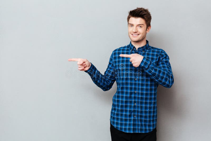 Attractive happy young man standing over grey wall and pointing royalty free stock image Attractive happy young man standing over grey wall and pointing royalty free stock image