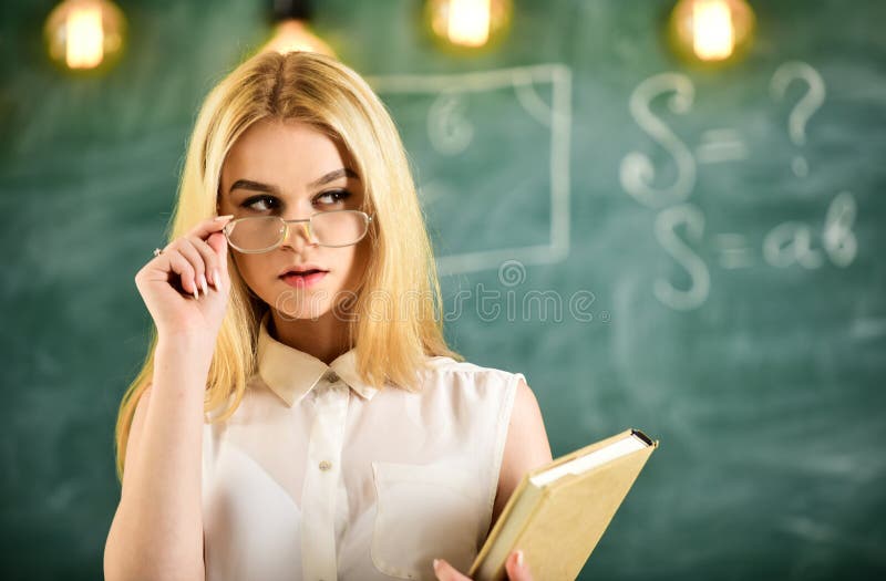 Attractive lecturer concept. Woman with book starts lesson, gazes at audience while taking off eyeglasses. Teacher looks royalty free stock photo Attractive lecturer concept. Woman with book starts lesson, gazes at audience while taking off eyeglasses. Teacher looks royalty free stock photo
