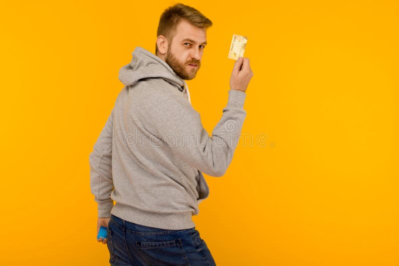 Attractive man in a gray hoodie points a finger at the credit card that is holding in his hand on a yellow background royalty free stock photos Attractive man in a gray hoodie points a finger at the credit card that is holding in his hand on a yellow background royalty free stock photos