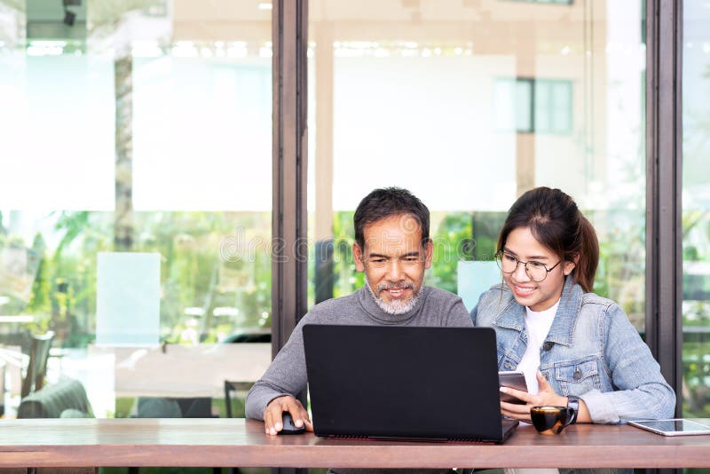 Attractive mature asian man with white stylish short beard looking at laptop computer with teenage eye glasses hipster woman in royalty free stock images Attractive mature asian man with white stylish short beard looking at laptop computer with teenage eye glasses hipster woman in royalty free stock images