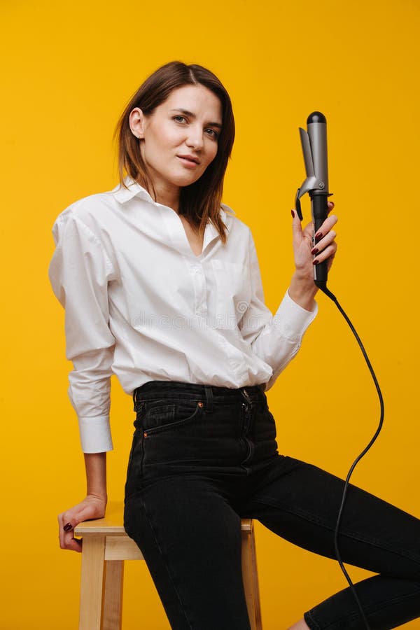 Attractive middle-aged stylist woman posing for a camera over yellow