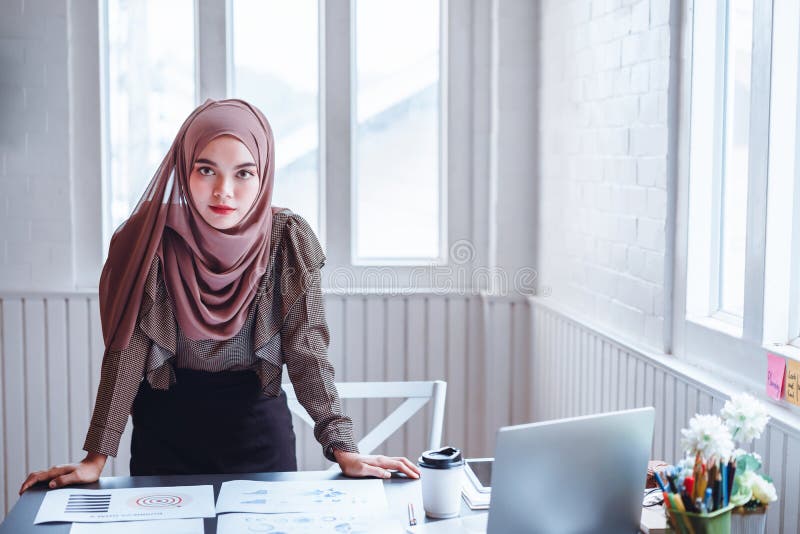 Attractive modern Arabic business woman in brown hijab at office workplace. Arab woman worker concept
