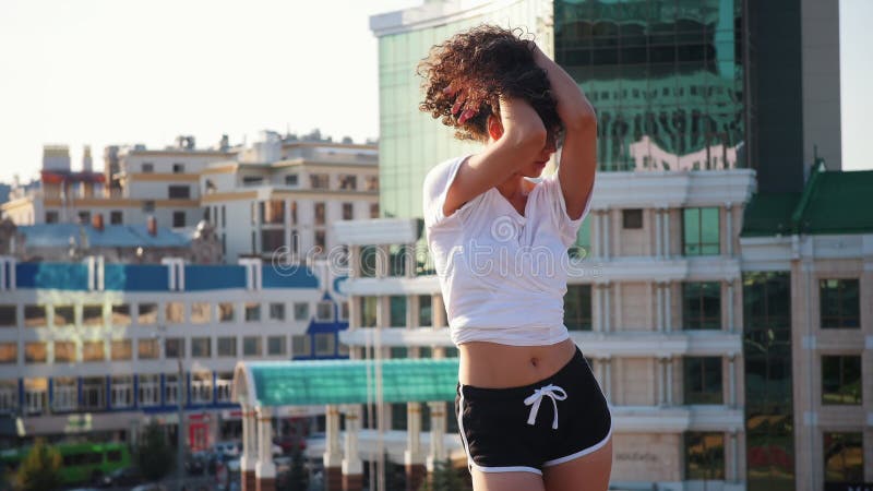 Attractive mulatto young woman with curly hair sexy dancing on high heels on the roof