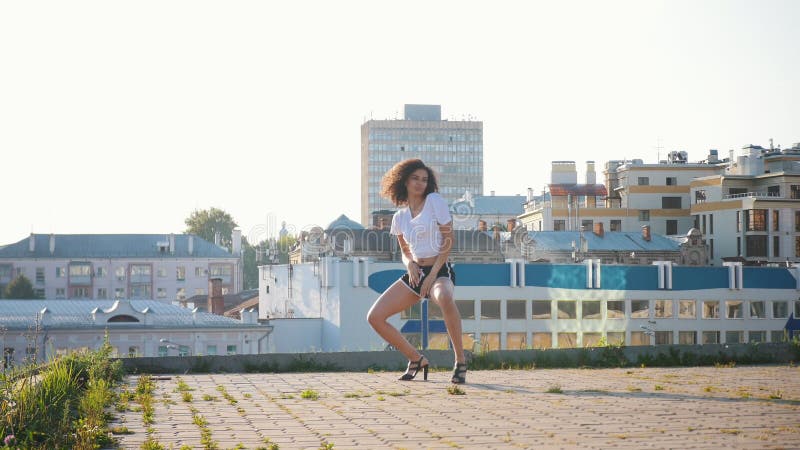 Attractive mulatto young woman sexy dancing on high heels on the roof