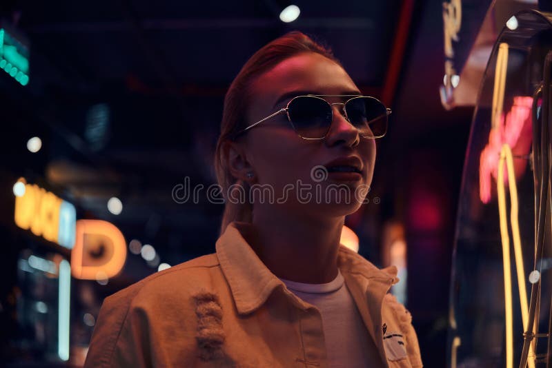 Attractive styilish woman is posing for photographer in neon lights. There are darkness at background. stock photography Attractive styilish woman is posing for photographer in neon lights. There are darkness at background. stock photography