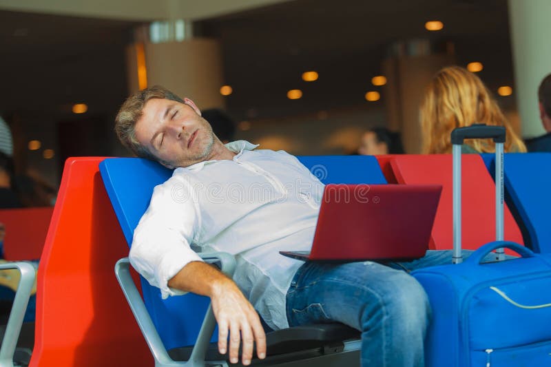 Young attractive and tired traveler man with luggage taking a nap sleeping while working with laptop computer waiting for flight at airport departure lounge in business trip concept