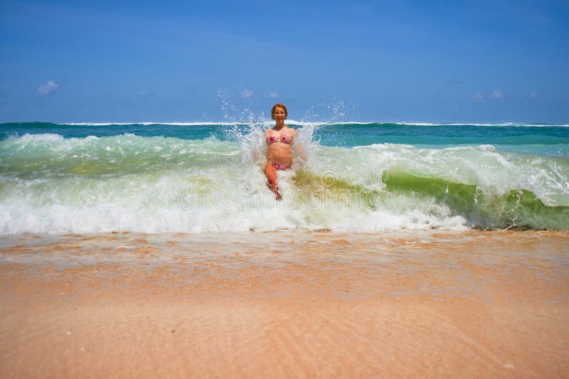 Attractive woman in bikini at amazing beautiful desert beach playing with big waves splashing and enjoying Summer holidays travel