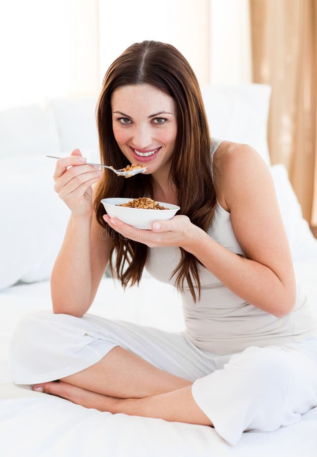 Attractive woman eating cereals sitting on bed at home