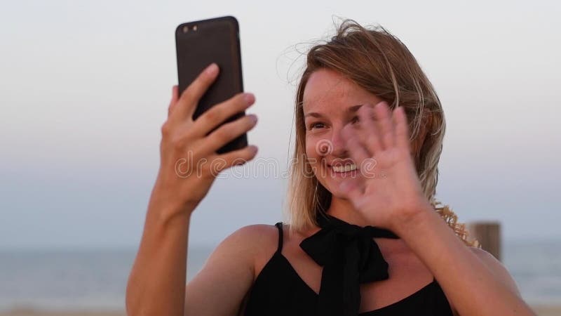 Attractive woman having video chats using smartphone. Portrait of happy woman smiling enjoying vacation on the beach in slow motio