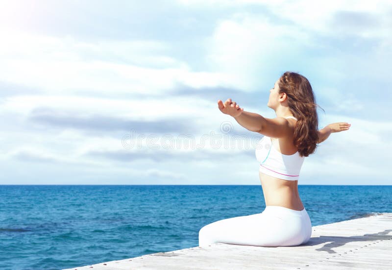 Attractive woman in white sporty clothes doing yoga on a wooden