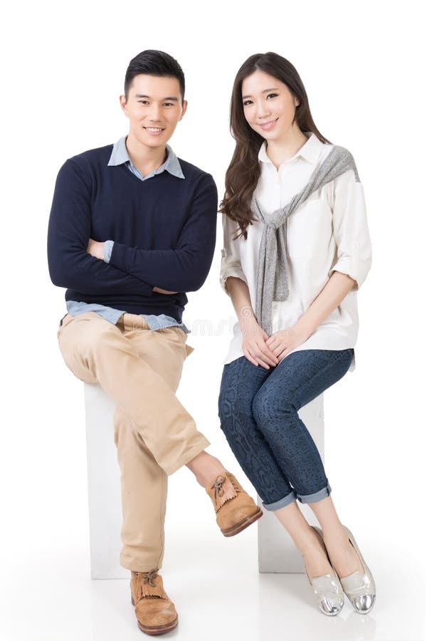 Attractive young Asian couple sit on boxes, full length portrait on white background.