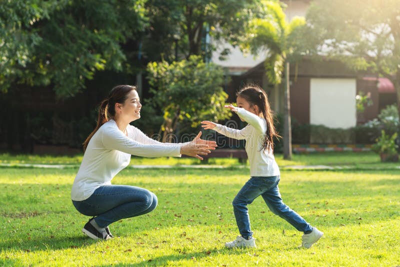 Attractive young asian mother and little cute girl daughter run to hug her mom in garden after back school in evening. Mom and royalty free stock photos Attractive young asian mother and little cute girl daughter run to hug her mom in garden after back school in evening. Mom and royalty free stock photos