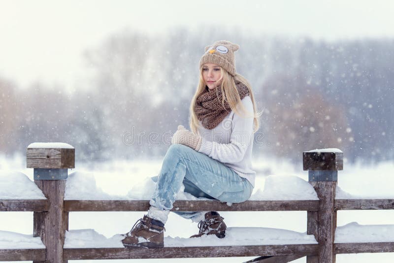 Attractive young blonde girl walking in winter forest. Pretty woman in wintertime outdoor. Wearing winter clothes. Knitted sweater