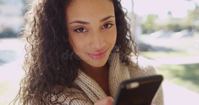 Attractive young brunette on a cell phone smiling at camera