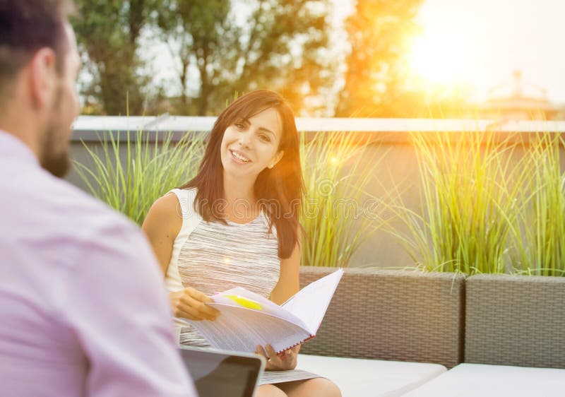 Attractive young business woman holding a file and smiling whilst she has a meeting outside wth a colleague who is working on his stock images Attractive young business woman holding a file and smiling whilst she has a meeting outside wth a colleague who is working on his stock images