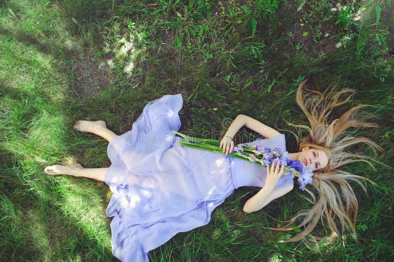 Atraktivní mladý blondýnka vlasy a přírodní vonící modrý purpurová kosatec květiny ležící na tráva venku, měkkost a měkkost na příroda.