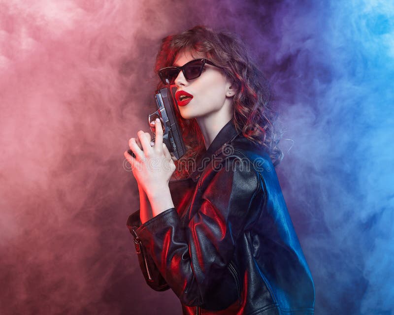 Attractive young girl with sunglasses and red lips poses with a gun
