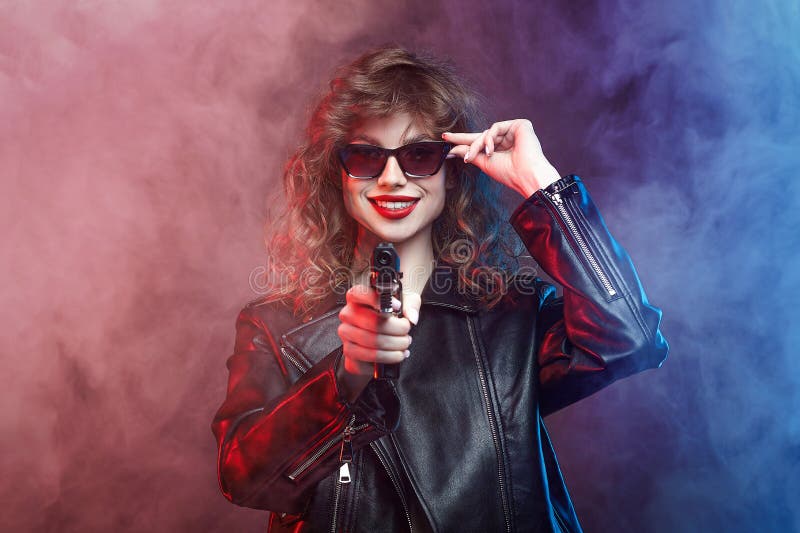 Attractive young girl with sunglasses and red lips poses with a gun