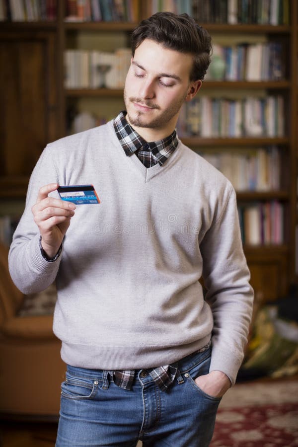 Attractive Young Man Holding Credit Card, Looking at it Stock Photo