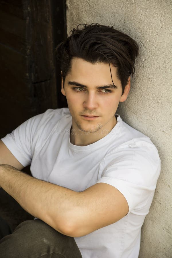 Attractive young man sitting on old door s threshold