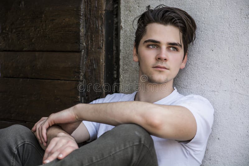 Attractive young man sitting on old door s threshold