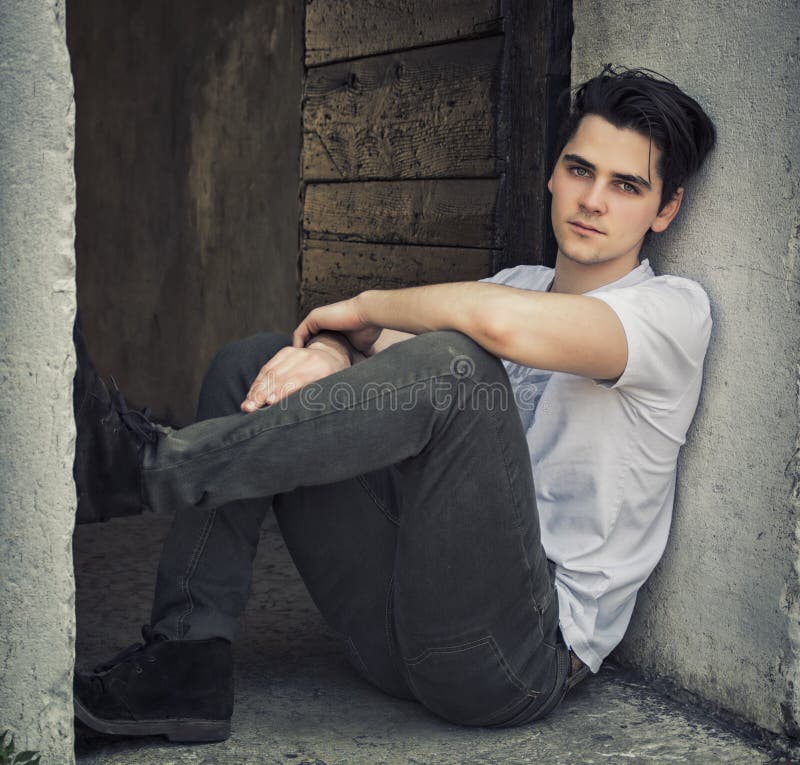Attractive young man sitting on old door s threshold