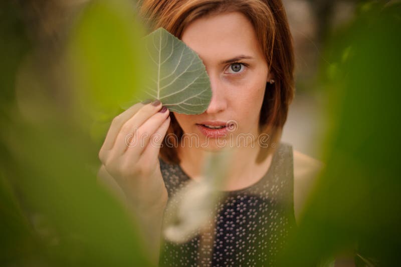 Attractive young redhead girl hiding a half of her face with green leaf royalty free stock image Attractive young redhead girl hiding a half of her face with green leaf royalty free stock image