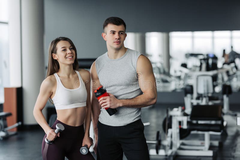 Attractive young sports people are holding bottle of water, talking and smiling while resting in gym royalty free stock photography Attractive young sports people are holding bottle of water, talking and smiling while resting in gym royalty free stock photography