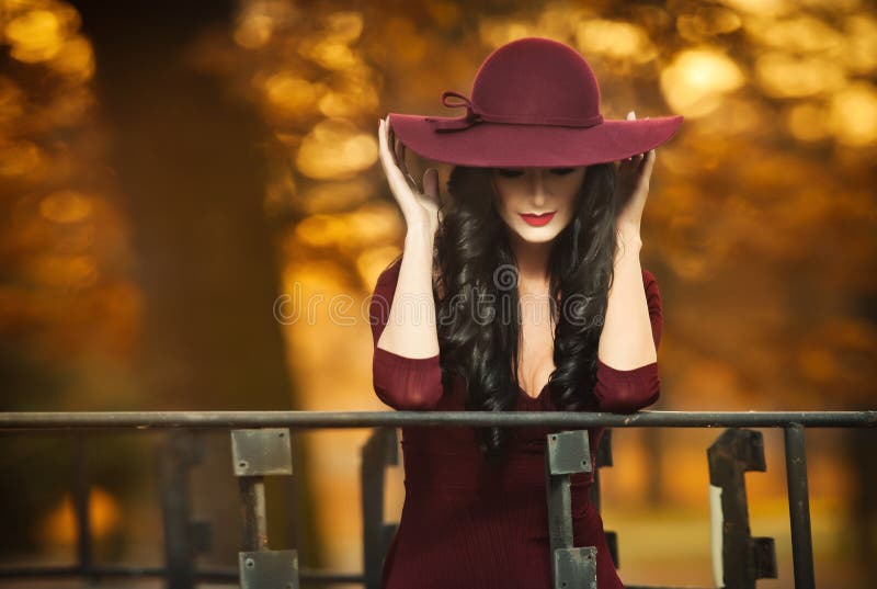 Attractive young woman with burgundy colored large hat in autumnal fashion shot. Beautiful mysterious lady covering the face