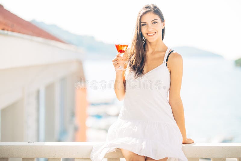 Attractive young woman drinking fruit alcoholic cocktail and enjoying her summer vacation.Holding glass of cold refreshing drink