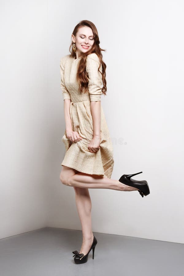 Attractive young woman in golden dress smiles and stands in fashion pose. She weares black high heels. She has long brown hair royalty free stock photography Attractive young woman in golden dress smiles and stands in fashion pose. She weares black high heels. She has long brown hair royalty free stock photography