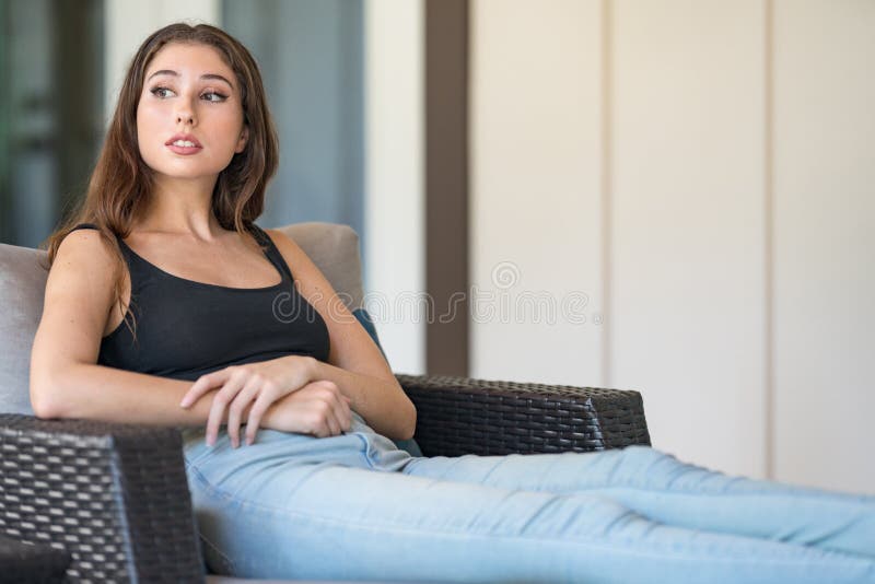 Attractive young woman posing on a wicker chair and looking away from camera