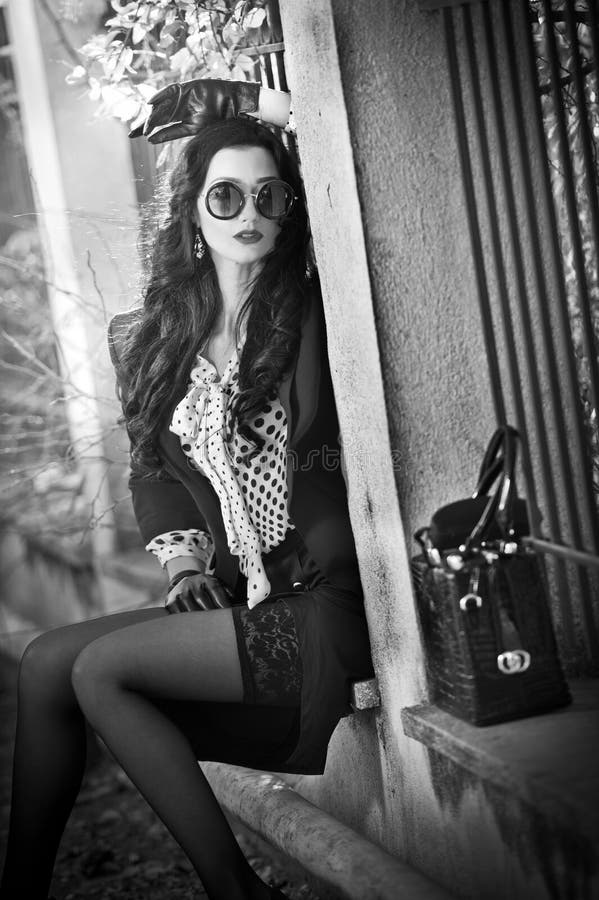 Attractive young woman with sunglasses in autumnal fashion shot. Beautiful lady in black and white outfit with short skirt sitting