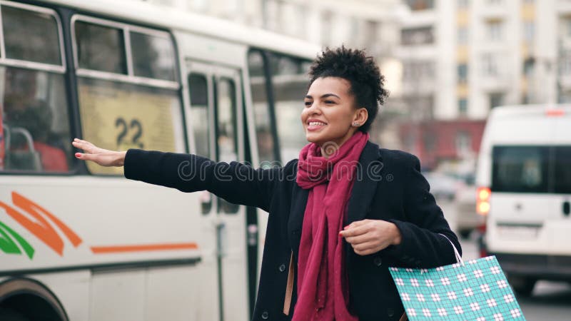 Attraktiv afrikansk amerikankvinna med shoppingpåsar som talar telefonen, medan vänta på taxitaxin och komma tillbaka från galler arkivbild Attraktiv afrikansk amerikankvinna med shoppingpåsar som talar telefonen, medan vänta på taxitaxin och komma tillbaka från galler arkivbild
