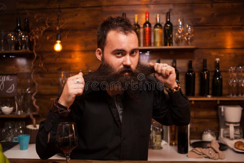 Attraktiv bartender som spelar med hans långa skägg bak räknaren royaltyfria foton Attraktiv bartender som spelar med hans långa skägg bak räknaren royaltyfria foton