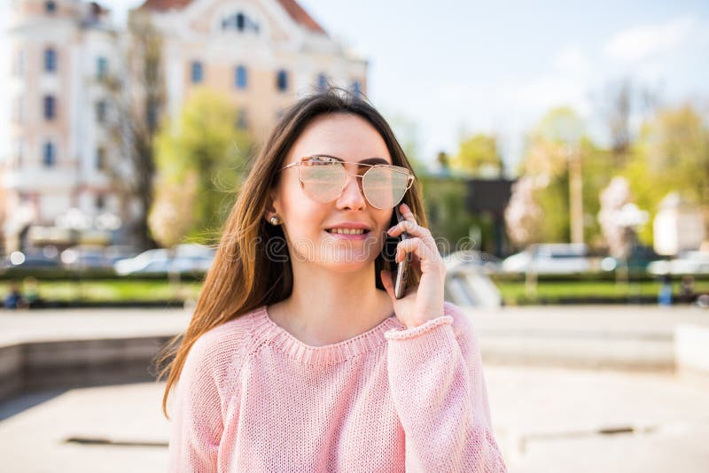 Attraktiv kvinna för stående i solglasögon på gatan som talar på telefonen och ler till kameran arkivbilder Attraktiv kvinna för stående i solglasögon på gatan som talar på telefonen och ler till kameran arkivbilder