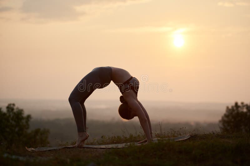 Attraktiv slank ung kvinna som utomhus gör yogaövningar på kopieringsutrymmebakgrund av härlig himmel fotografering för bildbyråer Attraktiv slank ung kvinna som utomhus gör yogaövningar på kopieringsutrymmebakgrund av härlig himmel fotografering för bildbyråer