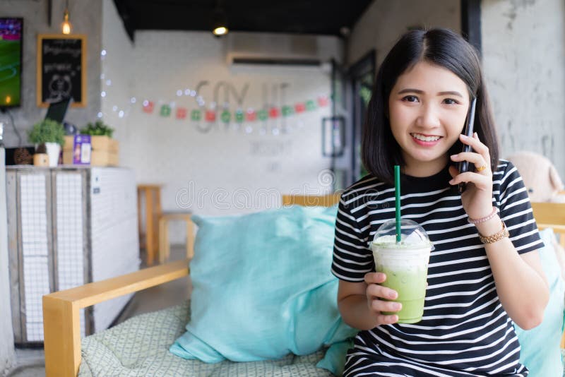 Attraktiv ung kvinna som talar på mobiltelefonen på coffee shop som dricker grönt te, medan sitta på soffan med den lyckliga ansi arkivbilder Attraktiv ung kvinna som talar på mobiltelefonen på coffee shop som dricker grönt te, medan sitta på soffan med den lyckliga ansi arkivbilder