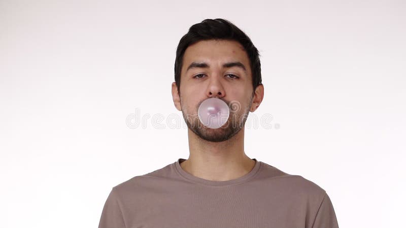 Attraktiva unga borstar som blåser tuggummibubbla med ögon som är öppna och isolerade över vit bakgrund Tuggummi