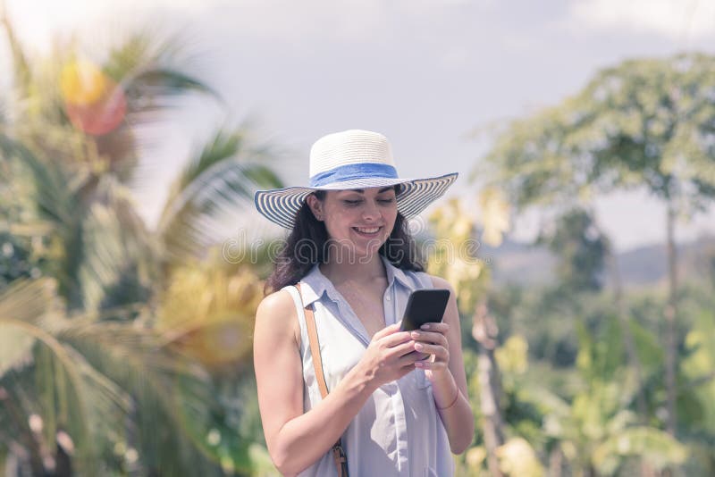 Attraktive Frau im Hut online verständigend mit Zellintelligentem Telefon über tropischem Forest View Young Girl Chatting stockbild Attraktive Frau im Hut online verständigend mit Zellintelligentem Telefon über tropischem Forest View Young Girl Chatting stockbild
