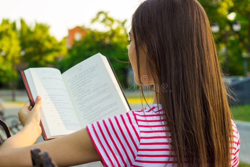 Attraktive Frau im roten und weißen T-Shirt ein Buch auf der Bank im Park am Sommertag genießend Hintere Ansicht eines junge Frau lizenzfreie stockfotos Attraktive Frau im roten und weißen T-Shirt ein Buch auf der Bank im Park am Sommertag genießend Hintere Ansicht eines junge Frau lizenzfreie stockfotos