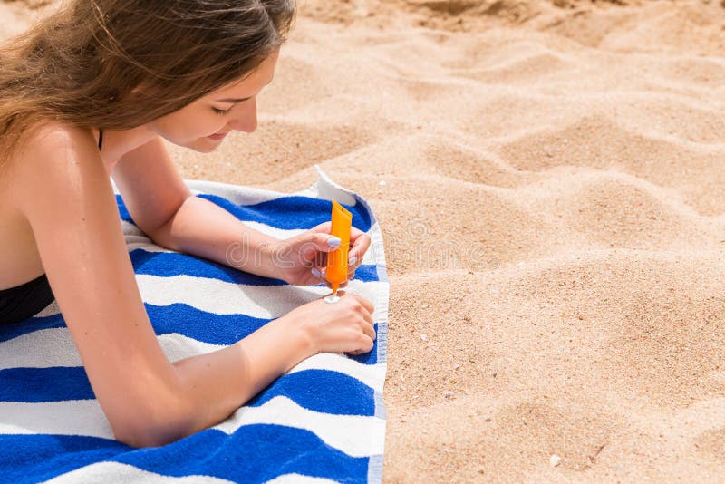 Attraktive Frau liegt auf einem gestreiften Tuch am Strand und drückt sunblock von einem Rohr auf ihrer Hand zusammen lizenzfreie stockbilder Attraktive Frau liegt auf einem gestreiften Tuch am Strand und drückt sunblock von einem Rohr auf ihrer Hand zusammen lizenzfreie stockbilder