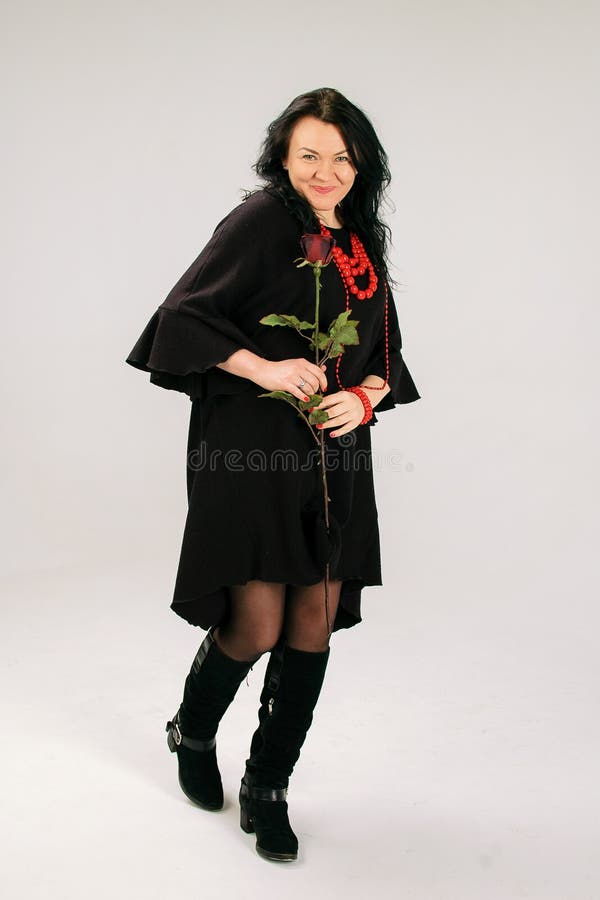 Attraktive Frau von mittlerem Alter mit roter Rose Dancing im Studio im schwarzen Kleid und in der ethnischen Halskette stockbilder Attraktive Frau von mittlerem Alter mit roter Rose Dancing im Studio im schwarzen Kleid und in der ethnischen Halskette stockbilder