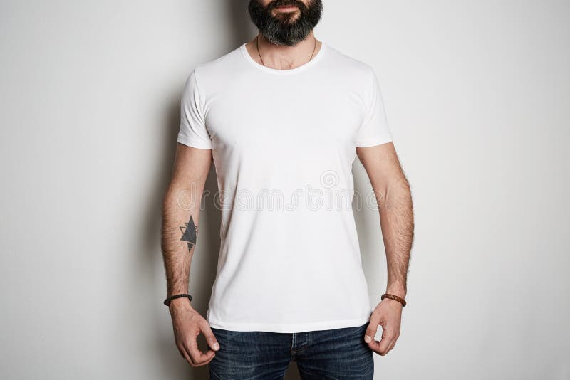 Attraktive grobe tätowierte bärtige Kerlhaltungen in den Blue Jeans und leeres graues T-Shirt in der erstklassigen Sommerbaumwo lizenzfreies stockbild Attraktive grobe tätowierte bärtige Kerlhaltungen in den Blue Jeans und leeres graues T-Shirt in der erstklassigen Sommerbaumwo lizenzfreies stockbild
