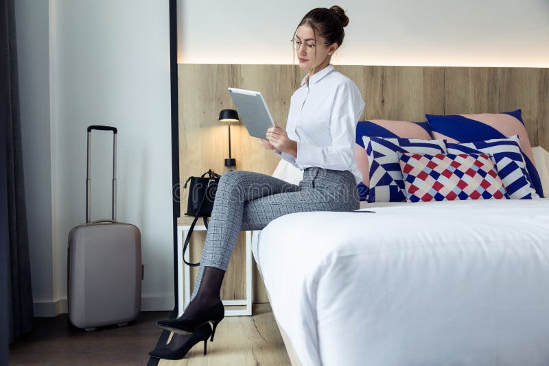 Attraktive junge Geschäftsfrau, die ihre digitale Tablette sitzt auf dem Bett am Hotelzimmer verwendet stockfotografie Attraktive junge Geschäftsfrau, die ihre digitale Tablette sitzt auf dem Bett am Hotelzimmer verwendet stockfotografie