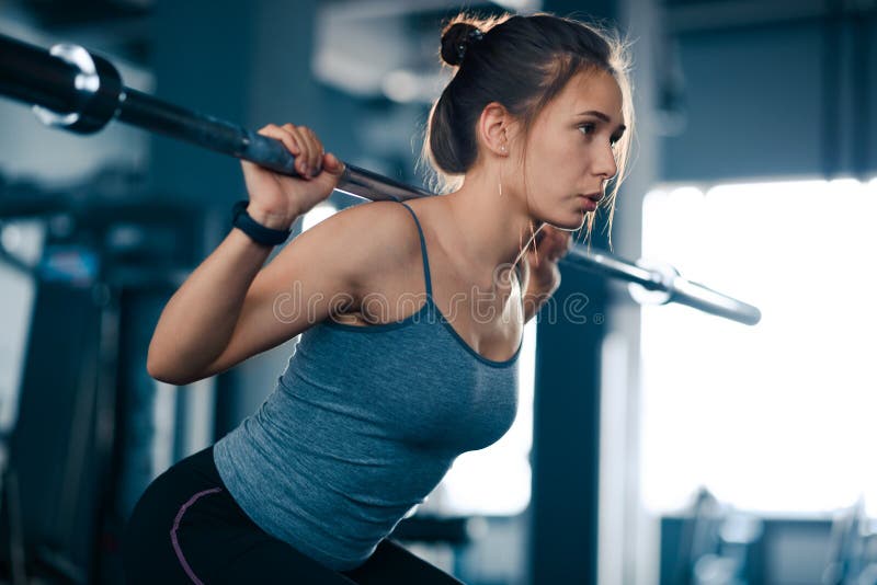 Attractive Young Sports Woman Doing Squats with Barbell in the Gym. Fitness and Healthy Lifestyle Concept. Attractive Young Sports Woman Doing Squats with Barbell in the Gym. Fitness and Healthy Lifestyle Concept.