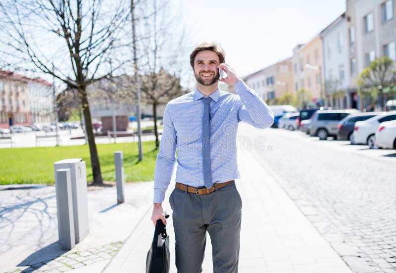 Handsome businessman phone calling on smartphone, standing in city street. Working remotely, waiting for business meeting. Manager smiling, outdoor in urban setting. Handsome businessman phone calling on smartphone, standing in city street. Working remotely, waiting for business meeting. Manager smiling, outdoor in urban setting.