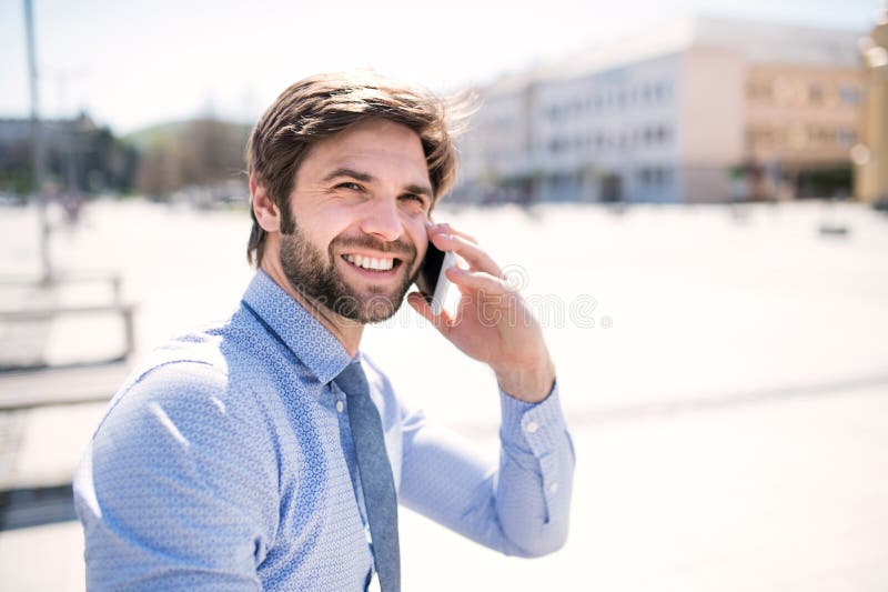 Handsome businessman phone calling on smartphone, standing in city street. Working remotely, waiting for business meeting. Manager smiling, outdoor in urban setting. Handsome businessman phone calling on smartphone, standing in city street. Working remotely, waiting for business meeting. Manager smiling, outdoor in urban setting.