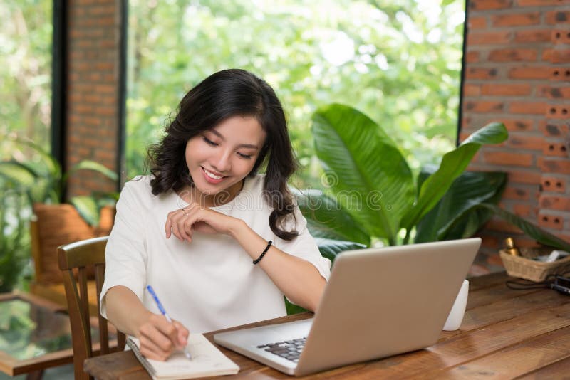 Attraktives Jung asiatisches Schreiben während des Laptops an der Kaffeestube stockfoto