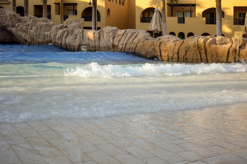 Attrazione acquatica nel cortile del comodo hotel egiziano con palme. Acqua pulita trasparente che si avvicina all'onda artificial immagine stock libera da diritti